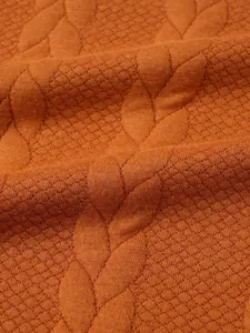 Macro detail of burnt orange jacquard knit fabric showing leaf pattern texture detail