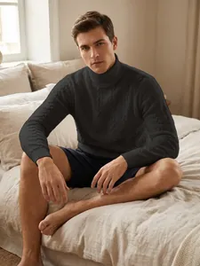 Model wearing a black men's cable knit turtleneck sweater in a bedroom setting.