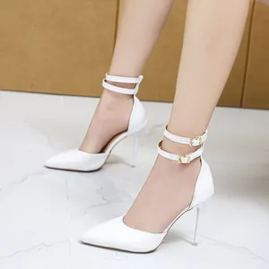 Close-up of elegant white pointed-toe stiletto heels featuring double gold buckle ankle straps.