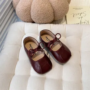 Close-up detail of vintage burgundy kids Mary Jane flat shoes on a cream cushion