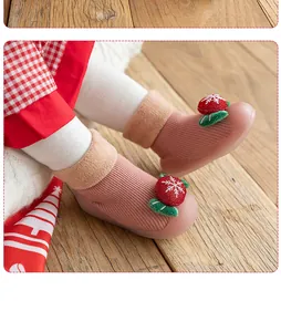 Detail of warm baby sock shoes with strawberry snowflake decoration on wooden floor.
