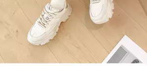 Stylish white women's chunky sneakers with thick soles shown on light wood floors