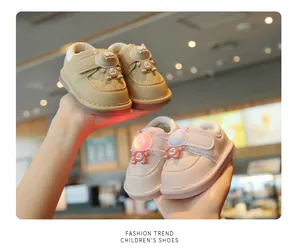 Hand-held close-up of khaki and pink baby light-up walking shoes with monster detail