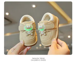 Close-up detail of beige infant walking shoes featuring a green glowing monster design