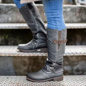 Close-up of women's grey riding boots with decorative belt buckle on metal stairs