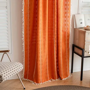 Detailed texture of orange semi-blackout curtain with white tassel trim and patterns