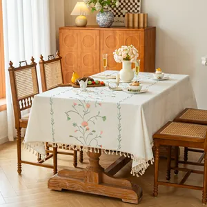 Elegant cream floral embroidered tablecloth with tassels on a rustic dining table