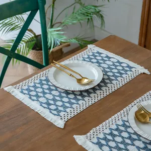 Detail shot of a blue diamond woven placemat with white tassels on a rustic wooden table.