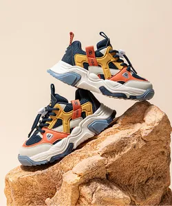 Multi-color chunky kids sneakers with pig-nose buckles displayed on a rock