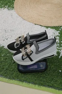 Detalle de mocasines fly-knit en blanco y negro con hebilla metálica sobre una báscula