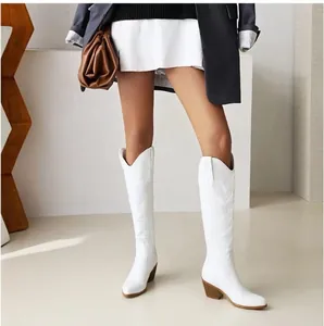 Detail of white embroidered V-cut western cowboy boots with a chunky heel on a model.