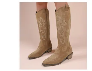 Detail view of brown suede cowboy boots with elegant white embroidery patterns.