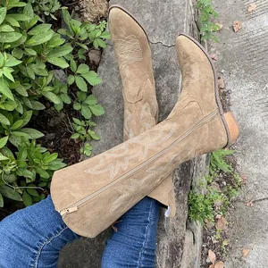 Detail of brown suede western boots with vintage embroidery on a stone background