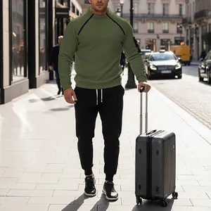 Male model walking in an olive green mock neck sweatshirt and joggers set with a suitcase