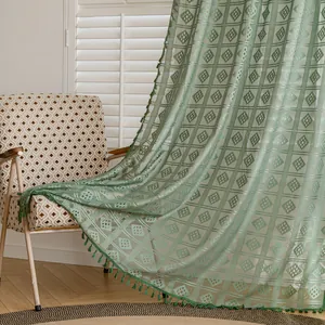 Dettaglio tenda in pizzo all'uncinetto verde con motivo geometrico a rombi e nappe decorative.