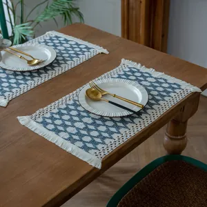 Blue diamond pattern woven placemats with fringe tassels displayed on a rustic wooden table
