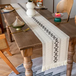 Chemin de table bohème en coton tissé avec pompons et motifs géométriques élégants.