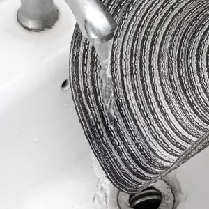Close-up of a round woven placemat being washed under a faucet in a sink