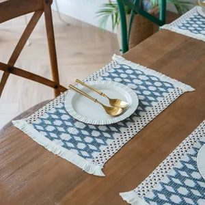Detail of a boho woven tasseled placemat with blue geometric pattern on a wooden table