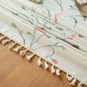 Close-up of elegant floral embroidery and tassel edge on a beige linen tablecloth.