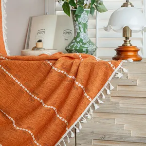 Close-up of orange textured curtain with white tassel fringe and woven patterns.