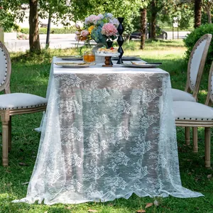 Detailed view of elegant white floral lace tablecloth at an outdoor garden party.