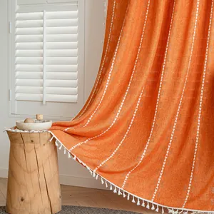 Close-up of orange semi-blackout curtain with white tassels and stitched patterns
