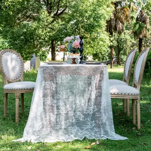 Close-up of white floral lace tablecloth on a wooden table in a garden setting.