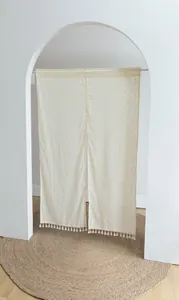 Detail view of a cream noren door curtain with yellow dots and tassel fringe in a bright room.