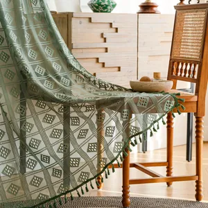 Dettaglio di tenda all'uncinetto verde con motivi geometrici e frange con nappe