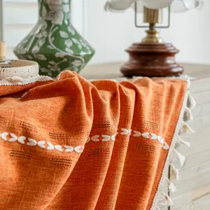 Close-up detail of orange semi-blackout curtain with white leaf embroidery and tassels.