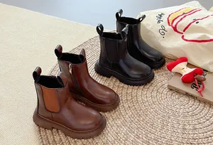 Detailweergave van bruine en zwarte Chelsea boots voor kinderen op een tapijt.