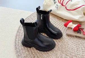 Stijlvolle zwarte Chelsea boots met dikke zool op een warm geweven vloerkleed nu.