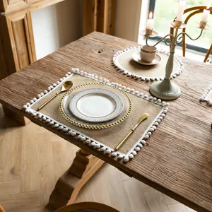 Farmhouse style rectangular jute placemat with white pom-pom tassels on rustic wood table