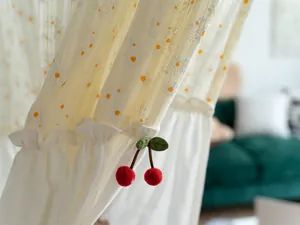 Close-up of white cotton door curtain with daisy print and red cherry charm detail