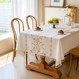 Elegant cream embroidered floral tablecloth with tassel edges in a bright dining room setting.