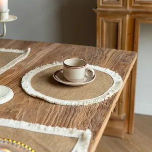 A detailed view of a round vintage farmhouse jute placemat with white fringe on a wooden table.