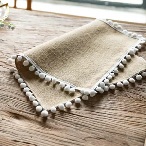 Detailed close-up of a farmhouse jute placemat with delicate white pom-pom tassel trim