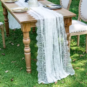 Elegant white lace table runner draped over a rustic wooden table in a garden setting.