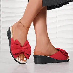 Mules à talons compensés rouges pour femmes avec grand nœud portées par un modèle
