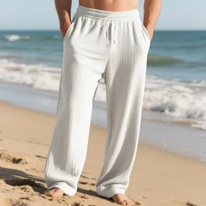 Detailed view of men's white ribbed wide-leg casual trousers with drawstring on beach