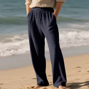 Detail of navy blue ribbed wide-leg pants with drawstring waist on a beach background.