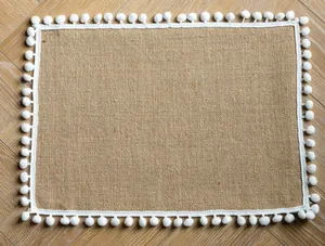 Detailed view of natural jute placemat featuring a white decorative pom-pom trim