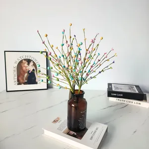 Colorful artificial berry branches displayed in a brown glass vase on decorative books