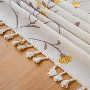 Close-up macro detail of embroidered floral tablecloth with decorative cream tassel fringe