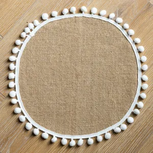Close-up detail of a round vintage burlap placemat featuring white pom-pom trim
