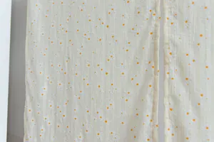 Close-up of white striped fabric curtain with delicate orange daisy embroidery details