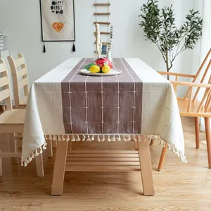 Detailansicht von Stickgitter und Quasten auf cremefarbener und brauner Tischdecke.