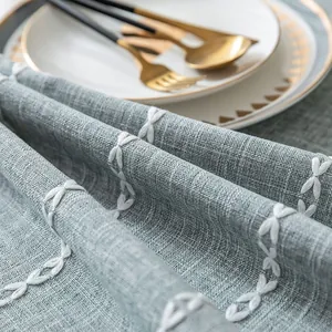 Detail of grey-blue linen-textured tablecloth with white cross-stitched embroidery.