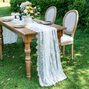 Elegant white lace table runner with floral embroidery shown in a rustic outdoor wedding scene.